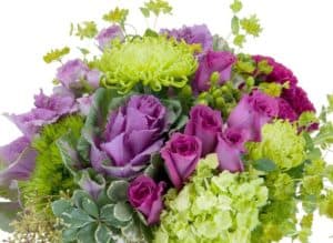 A magical mixture of magenta and green flowers, including roses, hydrangea, hypericum berry and ornamental kale, designed in a large clear glass vase.