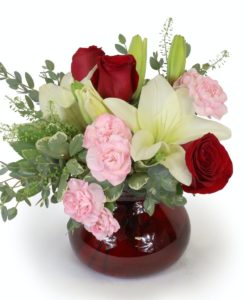 Send your modern day Juliet, her perfect bouquet! Filled with all the favorites of the season, Lilies, Roses and Carnations. With an assortment of premium greeneries and created in a ruby red vessel, it is sure to please. This compact style bouquet is great for a desk, at home or work. Romeo, send your Juliet this bouquet.