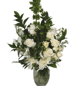 Beautiful white Roses in both full size and miniature mingle with fragrant Stock and Chrysanthemums. Deep green Bells of Ireland reach upwards and crown the design. Lush greenery is used throughout the design adding detail and softness. Created in a clear glass oval-shaped vase.